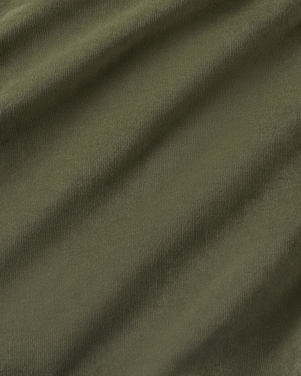 A close-up of olive green textured fabric with soft diagonal folds and shadows.