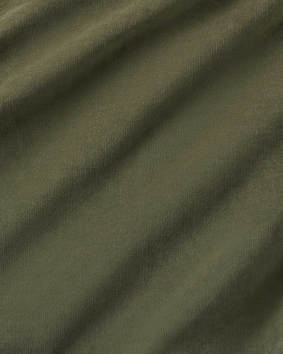 A close-up of olive green textured fabric with soft diagonal folds and shadows.