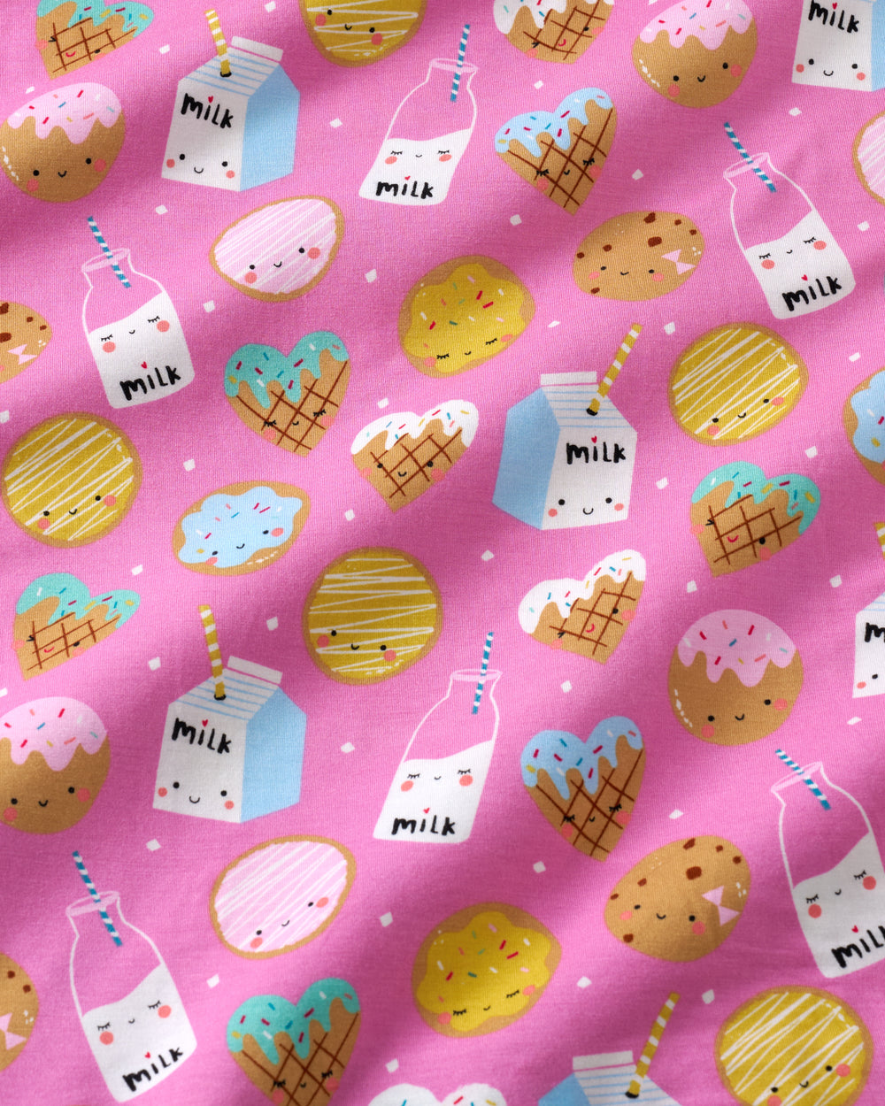A close-up of a pink patterned fabric featuring cute cartoon illustrations of milk cartons, milk bottles, cupcakes, ice cream cones, and cookies with smiling faces and small white polka dots.