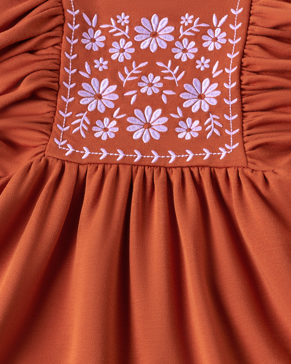 Close-up of a terracotta orange dress with floral embroidery on the bodice and gathered ruffles.