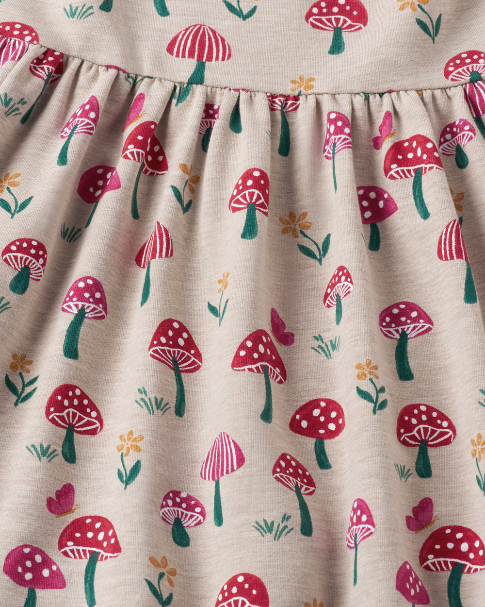 Close-up of a fabric product with a repeating mushroom print on a light beige background. The pattern features red and pink mushrooms with white spots, green stems, and small yellow flowers.