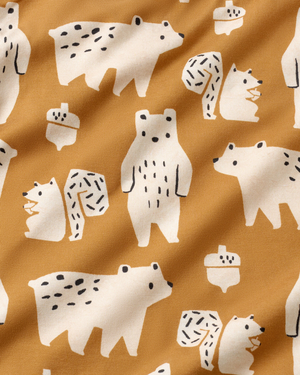 A close-up of a mustard yellow fabric with a repeating pattern of white cartoon bears, squirrels, and acorns with small black details.