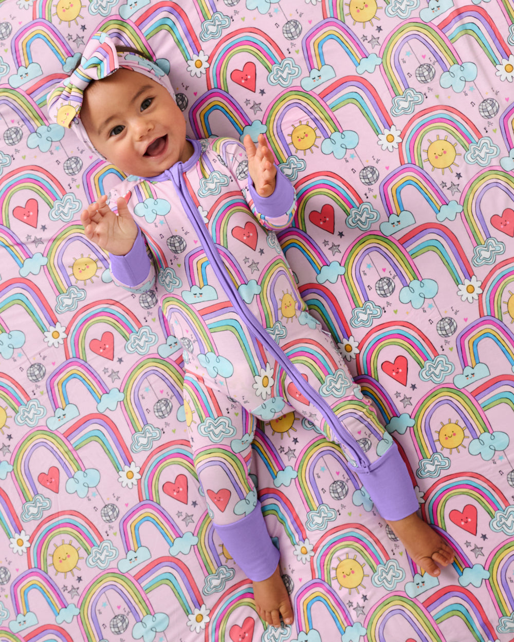 Aerial view of baby wearing the Disco Rainbows Zippy on a matching cloud blanket