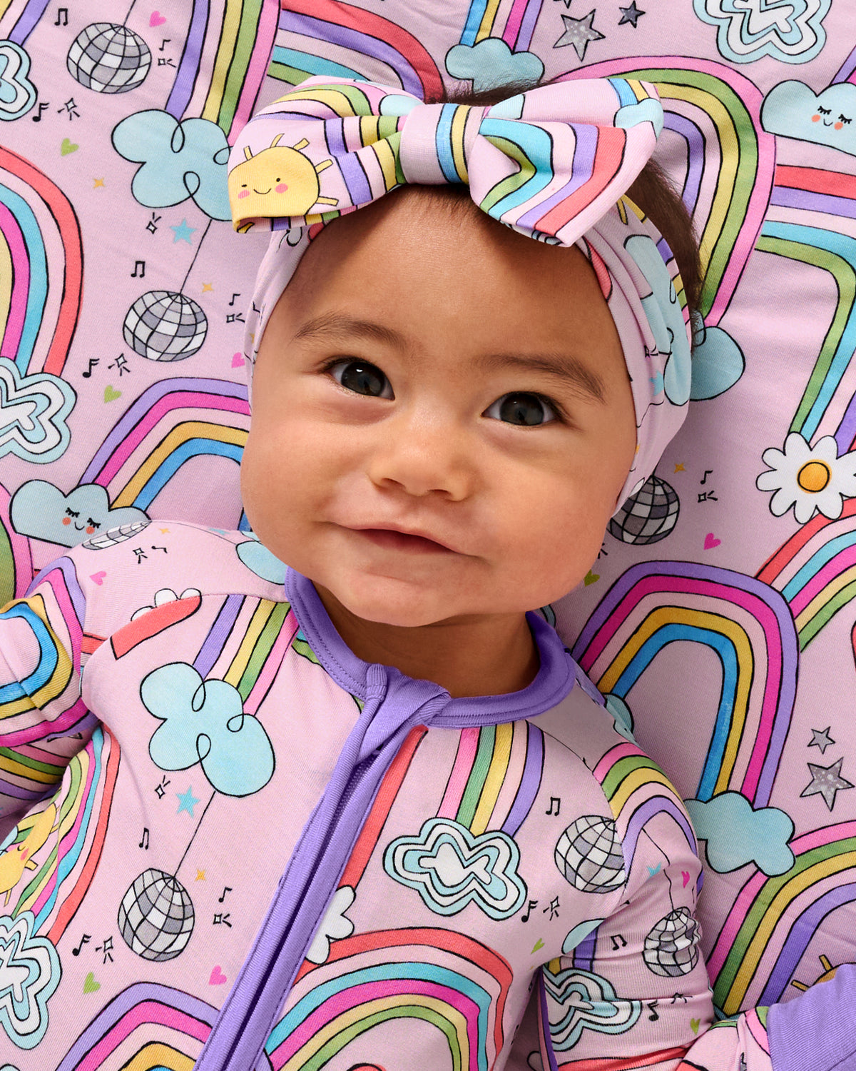 Aerial view of baby wearing the Disco Rainbows Luxe Bow Headband and matching zippy 