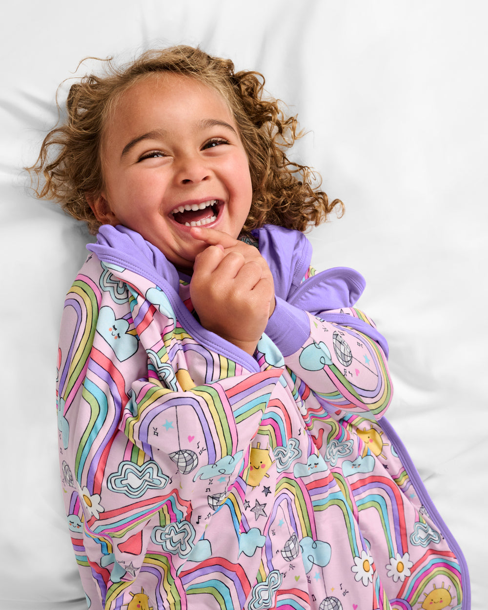 Child wrapped in the Disco Rainbows Large Cloud Blanket® on a white bed