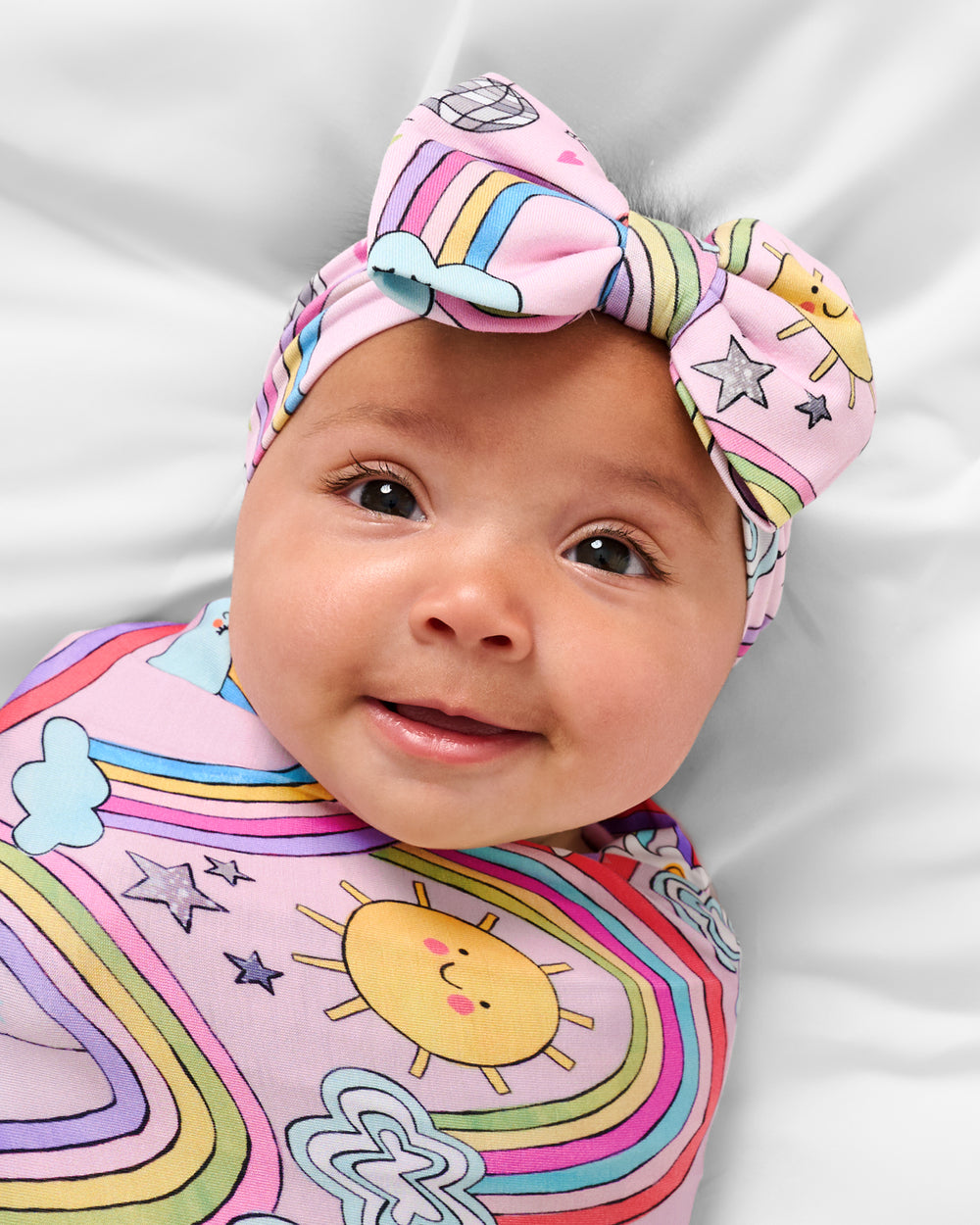 Close up of baby wearing the Disco Rainbows Swaddle & Luxe Bow Headband Set
