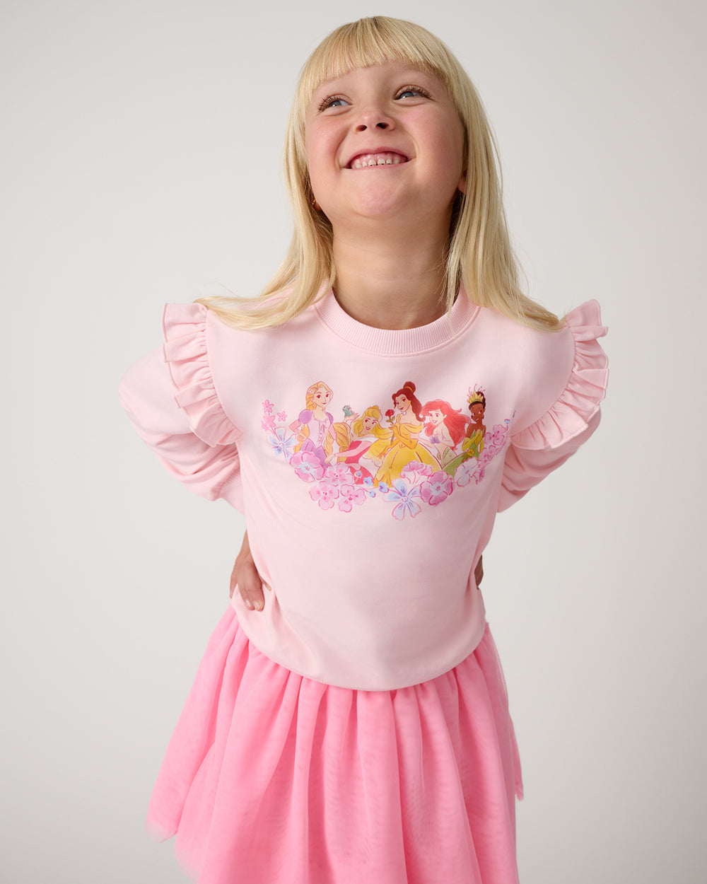 Girl wearing the Disney Floral Fairytale Flutter Crewneck with a pink skirt