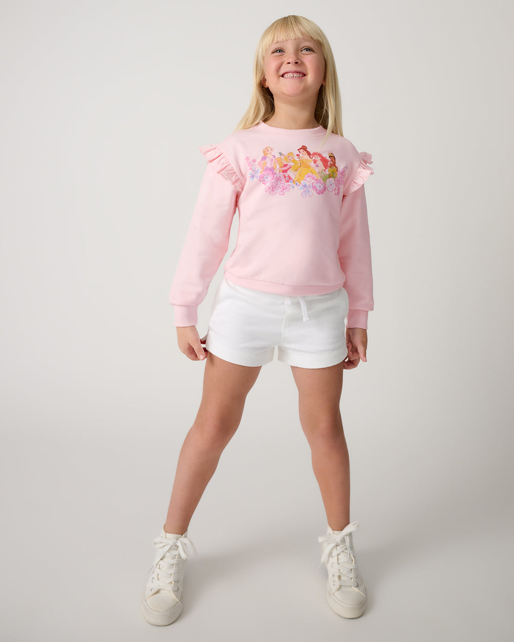 Girl wearig the Disney Floral Fairytale Flutter Crewneck with white shorts