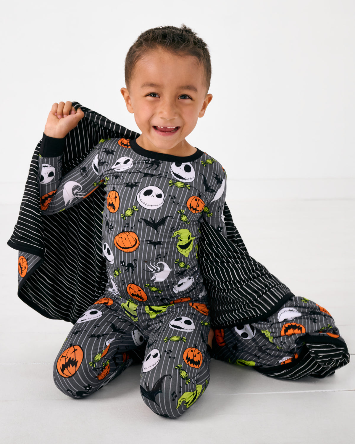 Sitting child wrapped in the Disney The Nightmare Before Christmas Large Cloud Blanket® wearing matching halloween pajamas