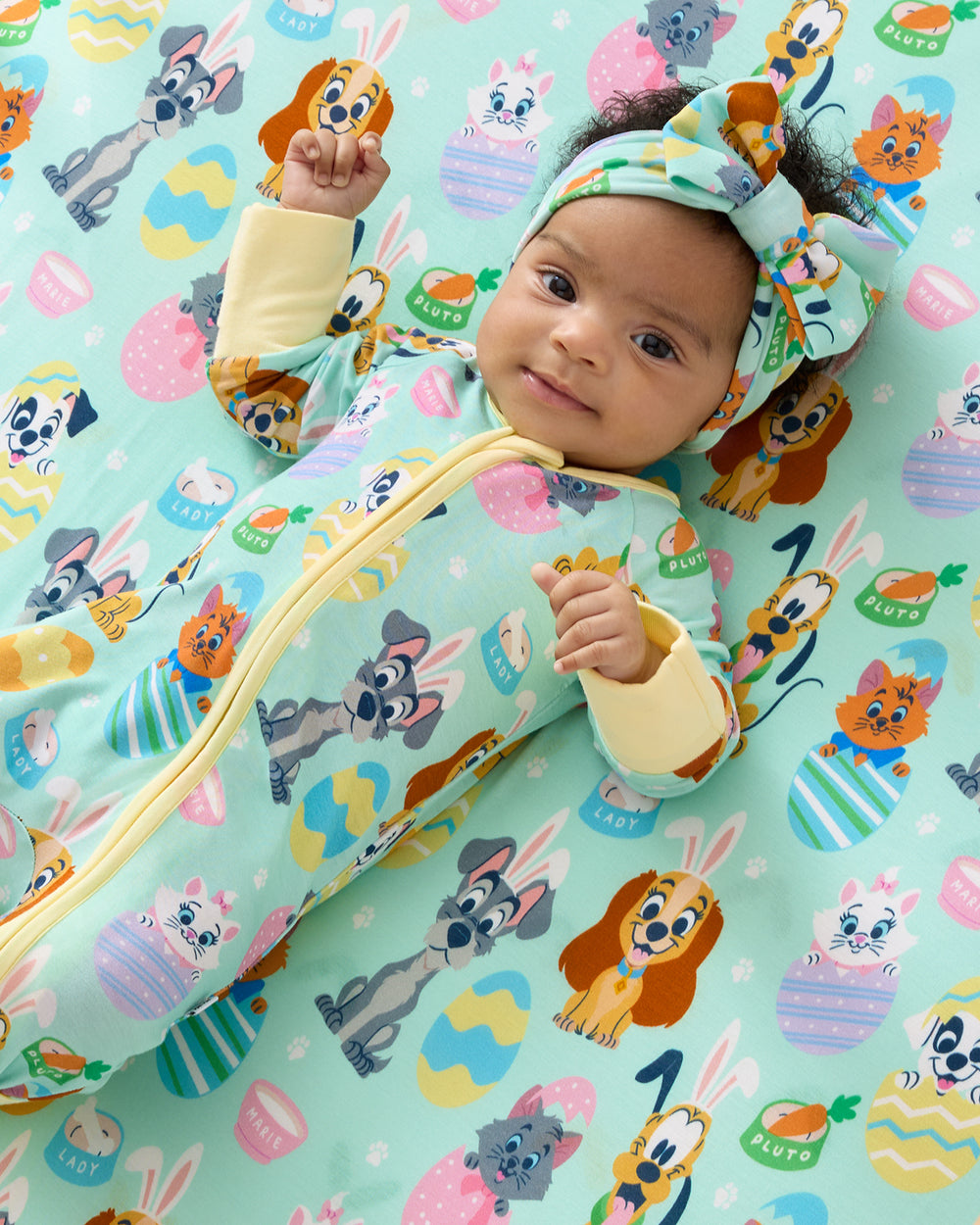 Close up of baby laying on the Disney Peekaboo Pets Fitted Crib Sheet in a matching zippy