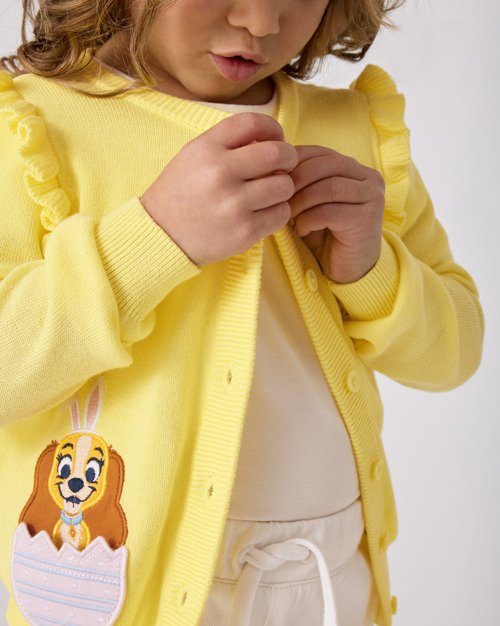Child buttoning up the Disney Peekaboo Pets Ruffle Cardigan