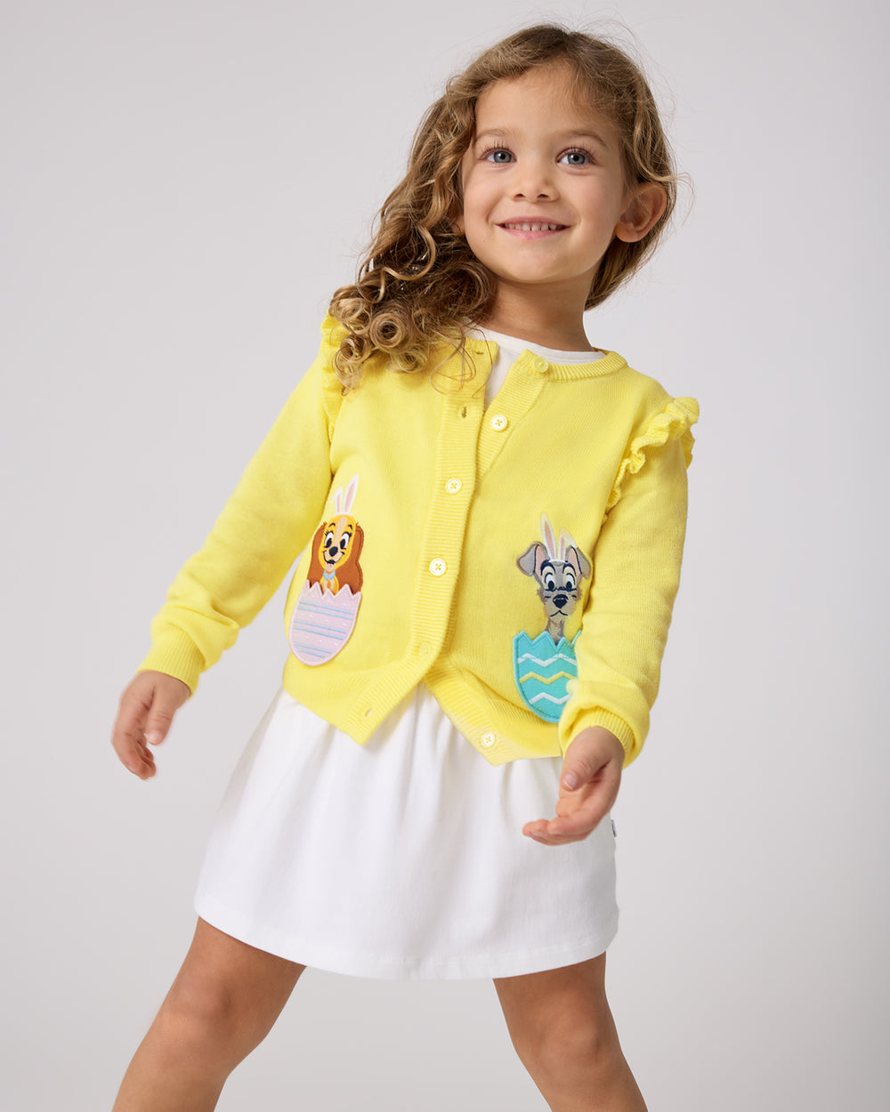 Girl wearing the Disney Peekaboo Pets Ruffle Cardigan with a white skort