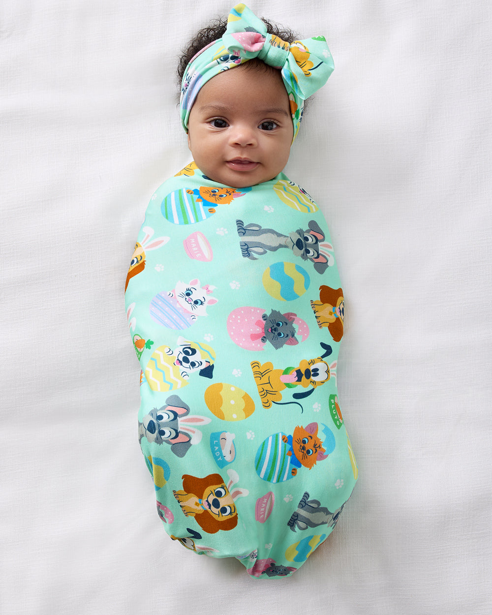 Aerial view of baby swaddled in the Disney Peekaboo Pets Swaddle & Luxe Bow Headband Set