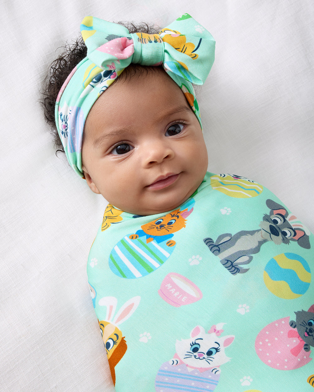 Close up of baby swaddled in the Disney Peekaboo Pets Swaddle & Luxe Bow Headband Set