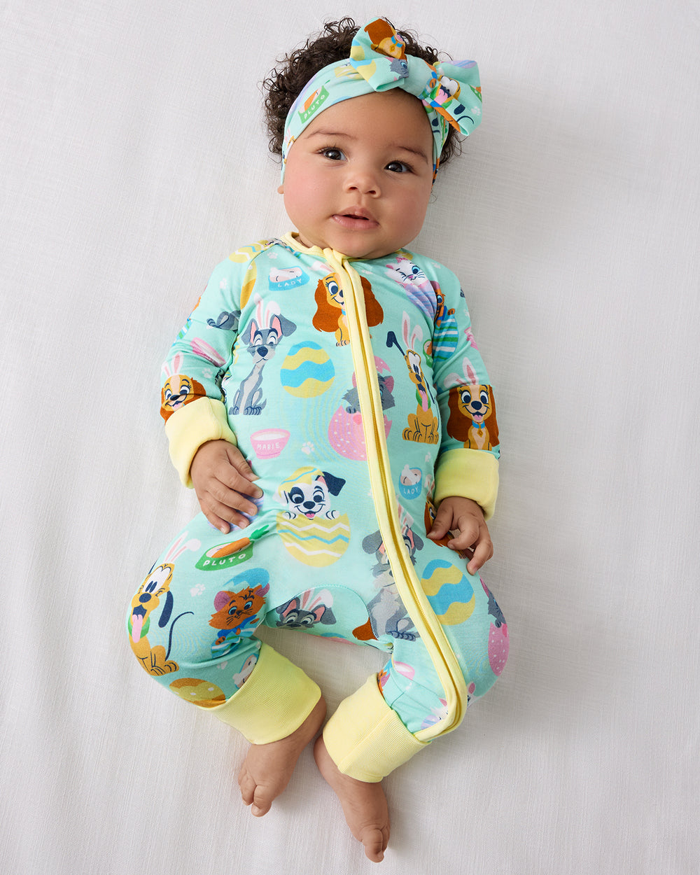 Aerial view of baby wearing the Disney Peekaboo Pets Luxe Bow Headband with a matching zippy