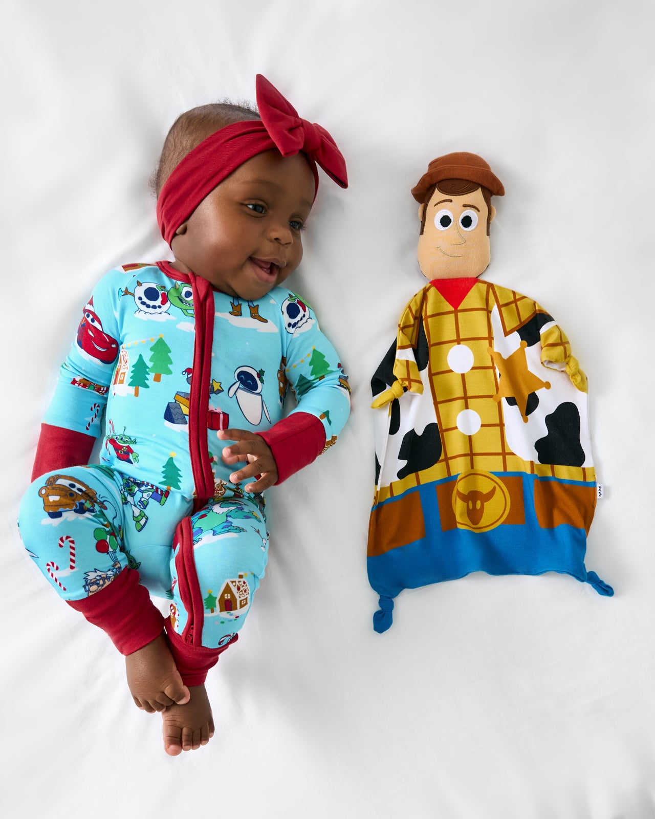 Baby wearing Disney holiday pajamas laying with the Disney Toy Story Woody Lovey
