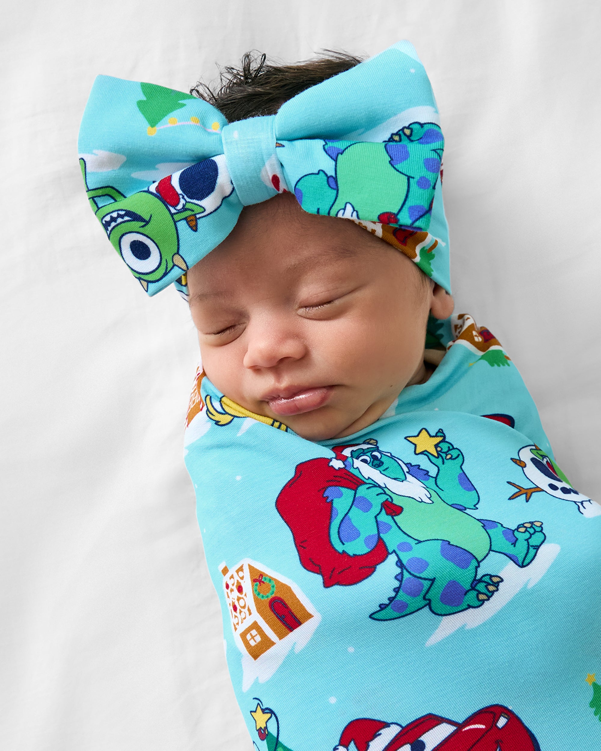 Close up of baby wearing the Disney & Pixar Christmas Village Swaddle & Luxe Bow Headband Set