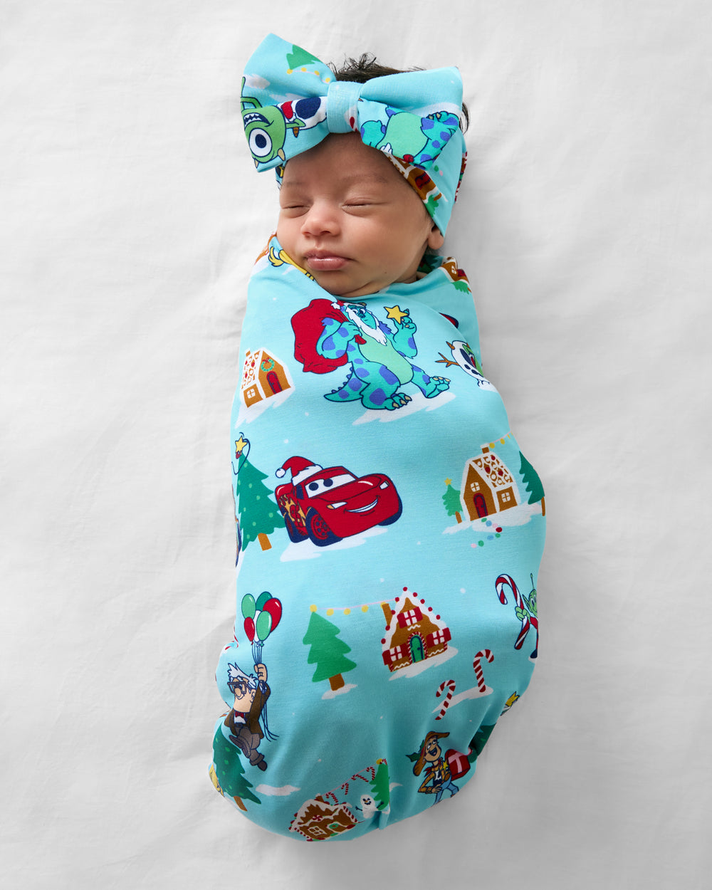 Aerial view of baby wearing the Disney & Pixar Christmas Village Swaddle & Luxe Bow Headband Set