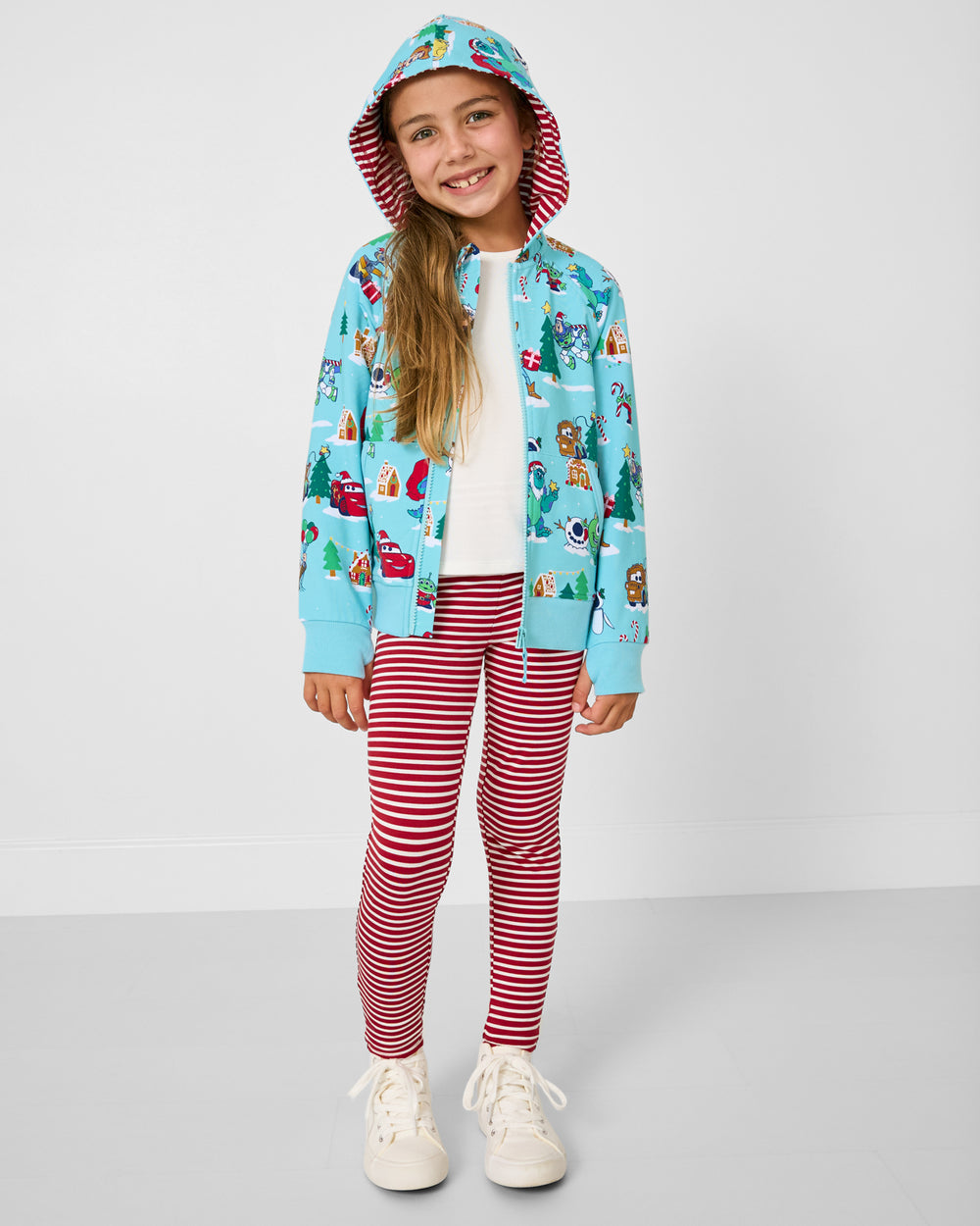 Child wearing the Disney & Pixar Christmas Village Zip Hoodie with red striped leggings