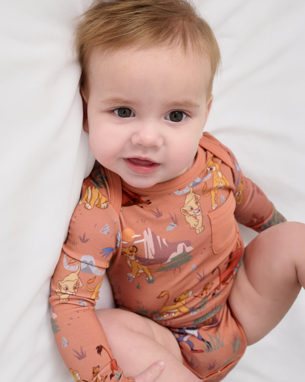 Close up of baby wearing the Disney Simba's Safari Pocket Bodysuit on a white bed