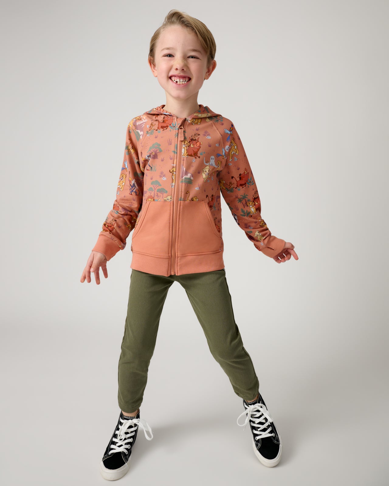 Standing boy wearing the Disney Simba's Safari Zip Hoodie with green jpggers