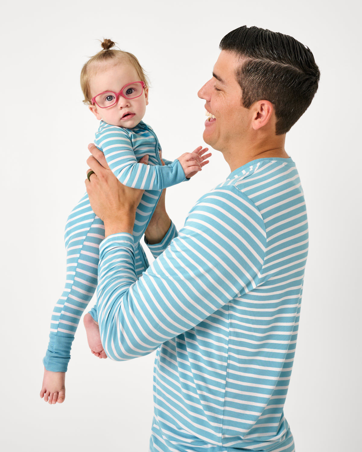 Father wearing the Dockside Stripe Men's Long Sleeve Pajama Top holding up a newborn in a matching footie