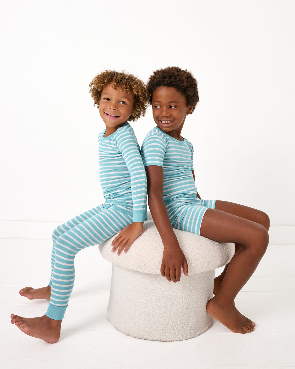 Two boys wearing matching Dockside Stripe Two-Piece Pajama Sets sitting on a boucle ottoman