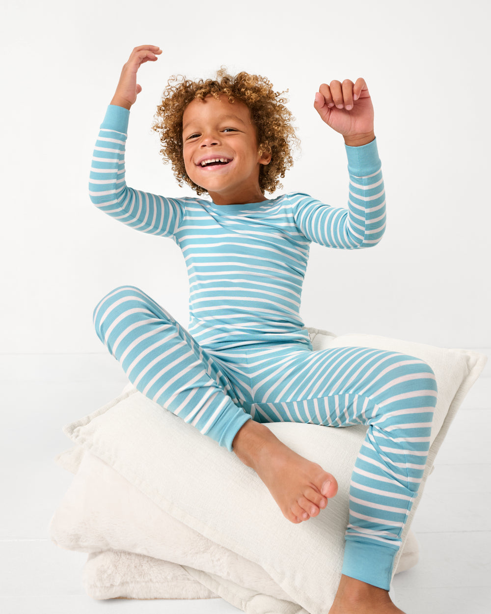 Boy sitting on a pile of pillows wearing the Dockside Stripe Two-Piece Pajama Set