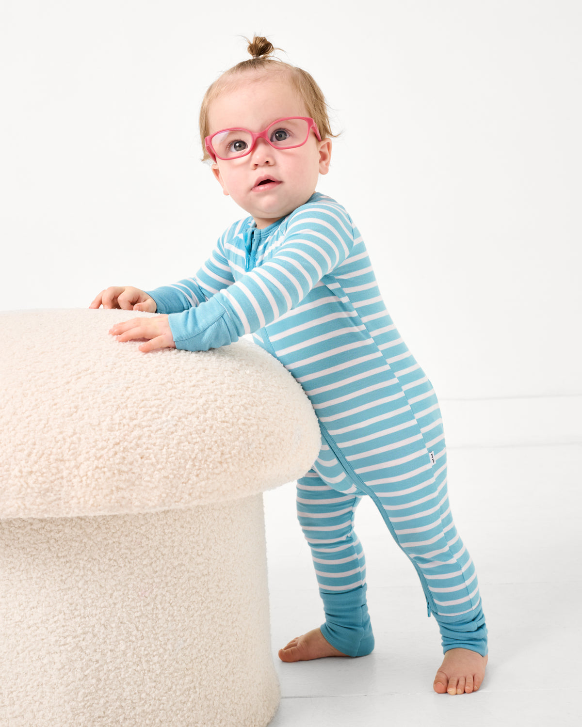 Baby leaning on a boucle ottoman wearing the Dockside Stripe Zippy