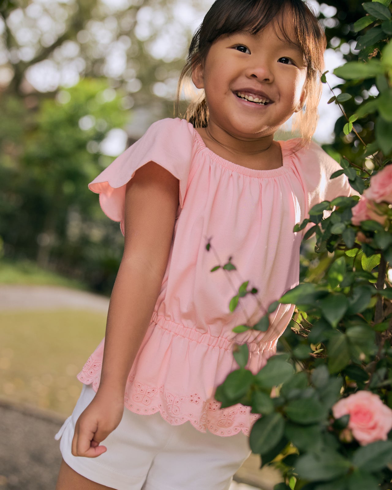 Girl wearing the Soft Coral Puff Sleeve Eyelet Top with a rose bush in the foreground