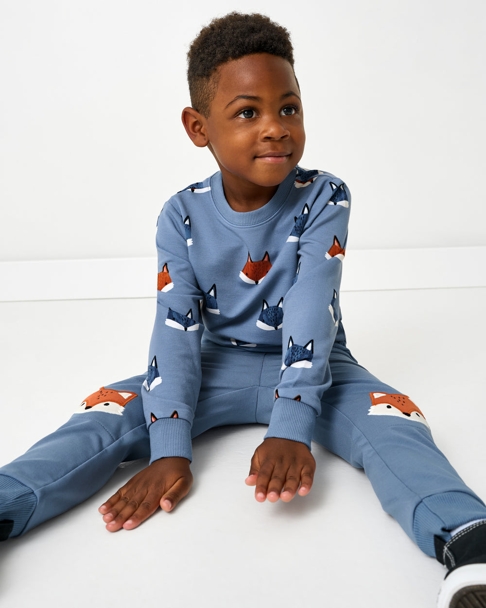 Sitting boy wearing the Fox Tracks Crewneck Sweatshirt with the coordinating sweatpants