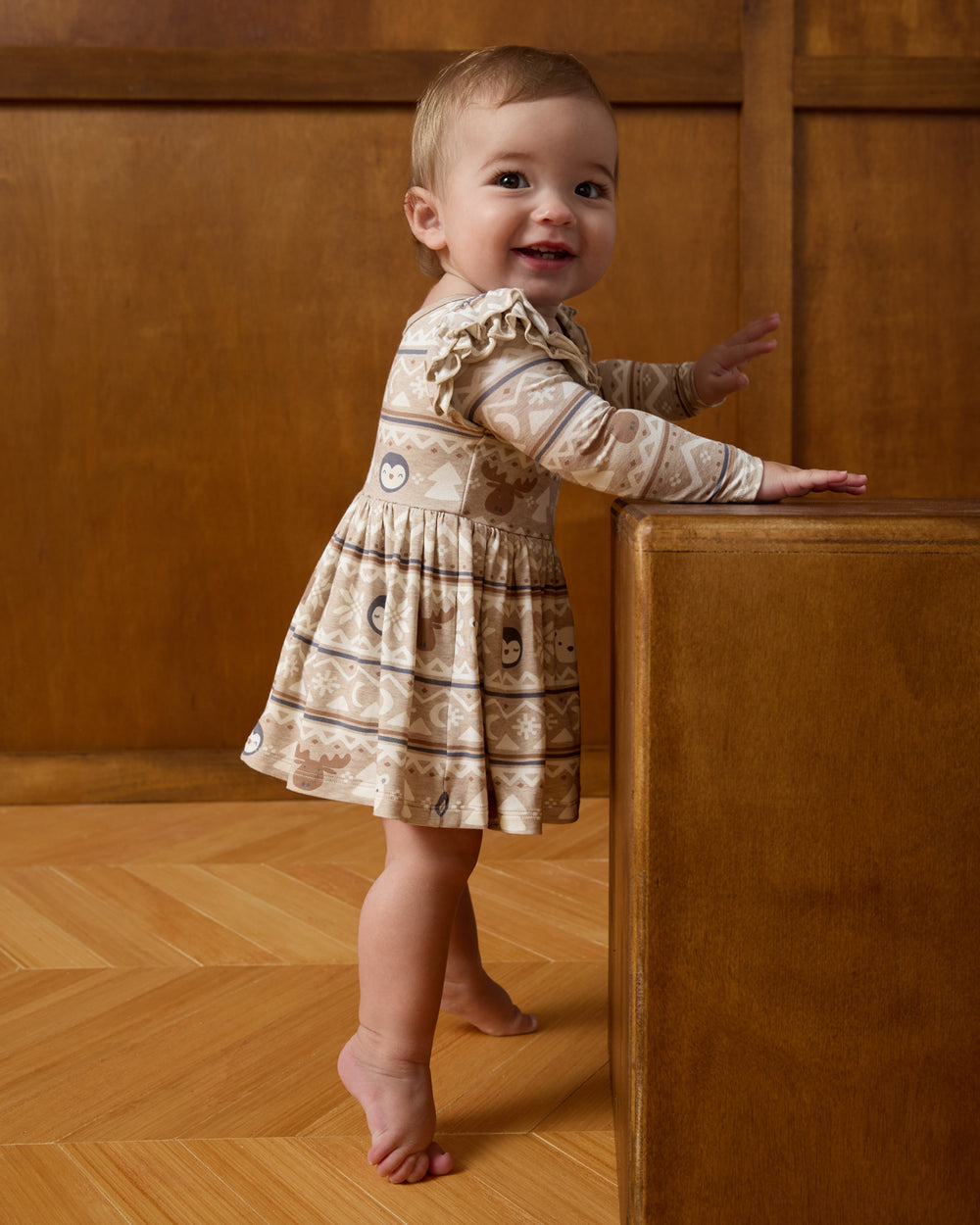 Baby wearing the Frosty Fair Isle Flutter Skater Dress with Bodysuit on a brown background