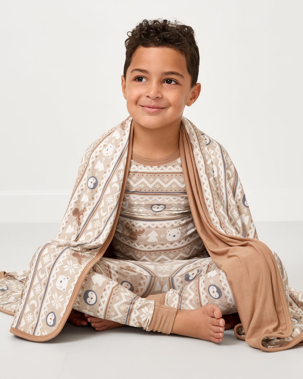 Sitting boy wrapped in the Frosty Fair Isle Large Cloud Blanket®
