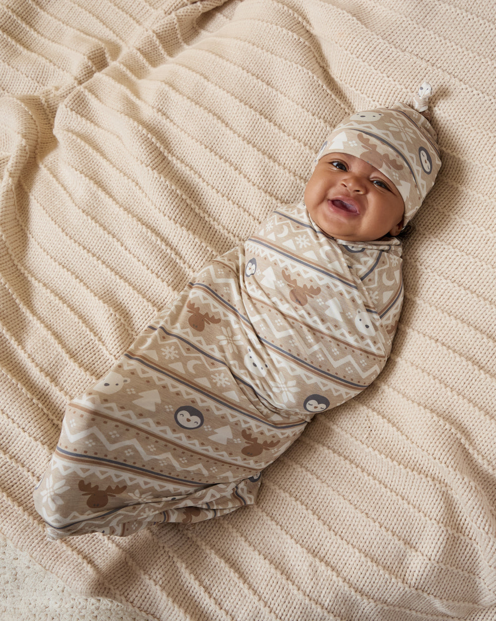 Aerial view of baby wearing the Frosty Fair Isle Swaddle & Hat Set on a knit blanket