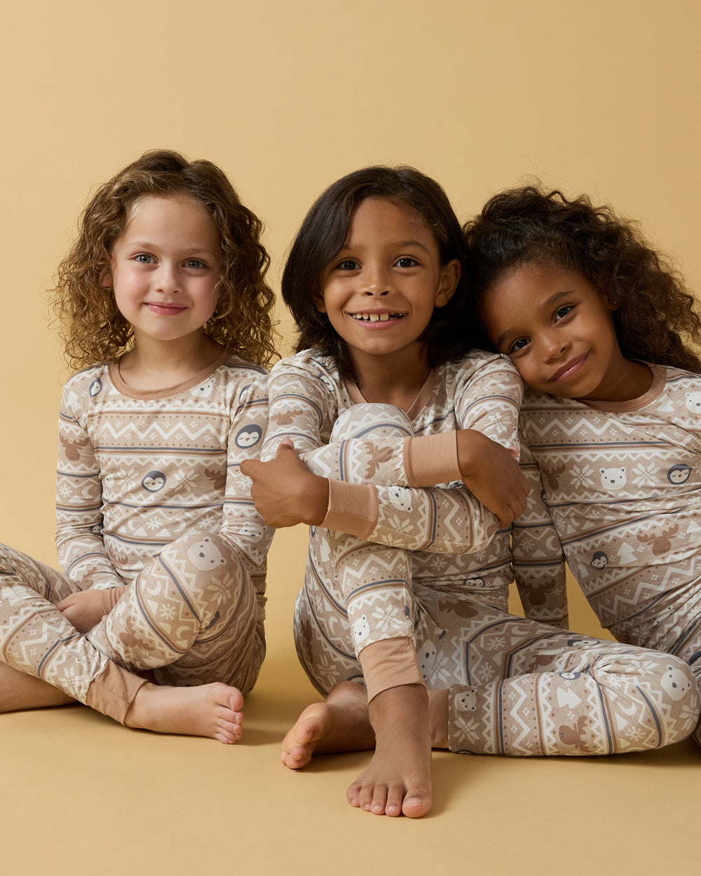Three girls wearing matching Frosty Fair Isle Two-Piece Pajama Sets on a yellow background