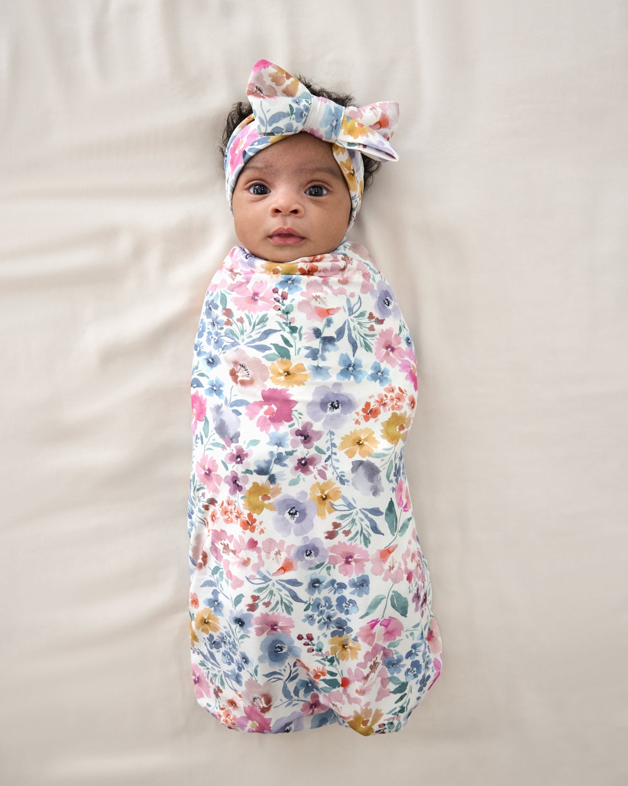Baby wrapped in the Tiny Blooms Swaddle & Luxe Bow Headband Set