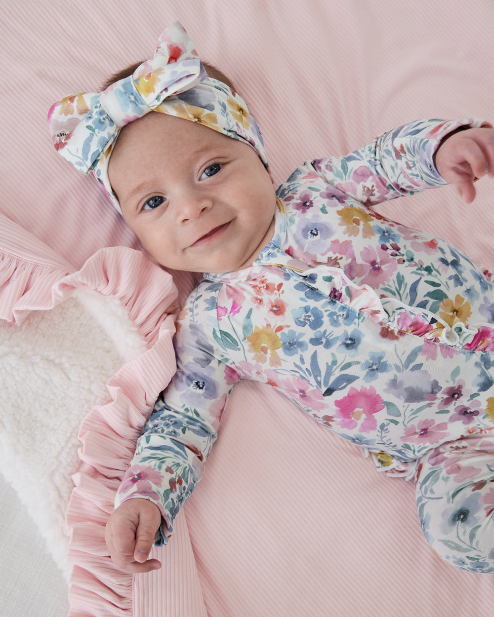 Baby wearing the Tiny Blooms Ruffle Zippy on a pink baby blanket