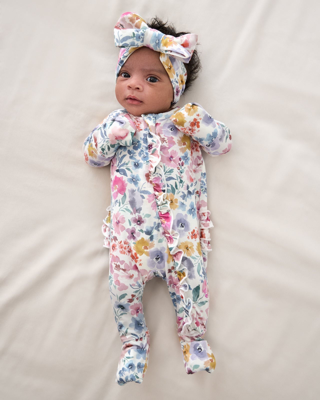 Newborn wearing the Tiny Blooms Ruffle Zippy with their feet and hands covered