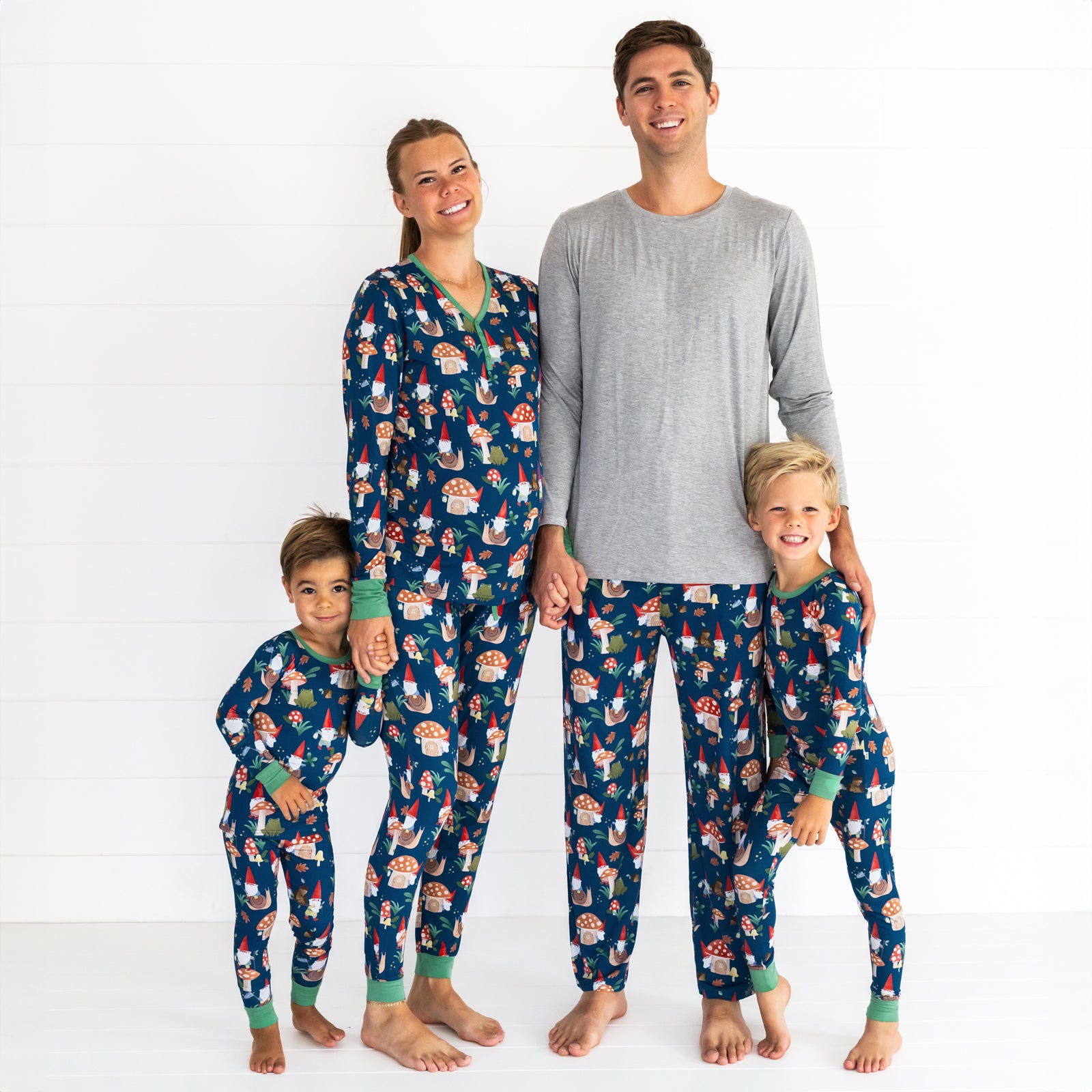 Family of four wearing the Forest Gnomes print. Male model is wearing the Forest Gnomes Men's Pajama Pant and female model is in the Forest Gnomes Women's Pajama Pant and Top. Both children are wearing the Forest Gnomes Two-piece Pajama Set