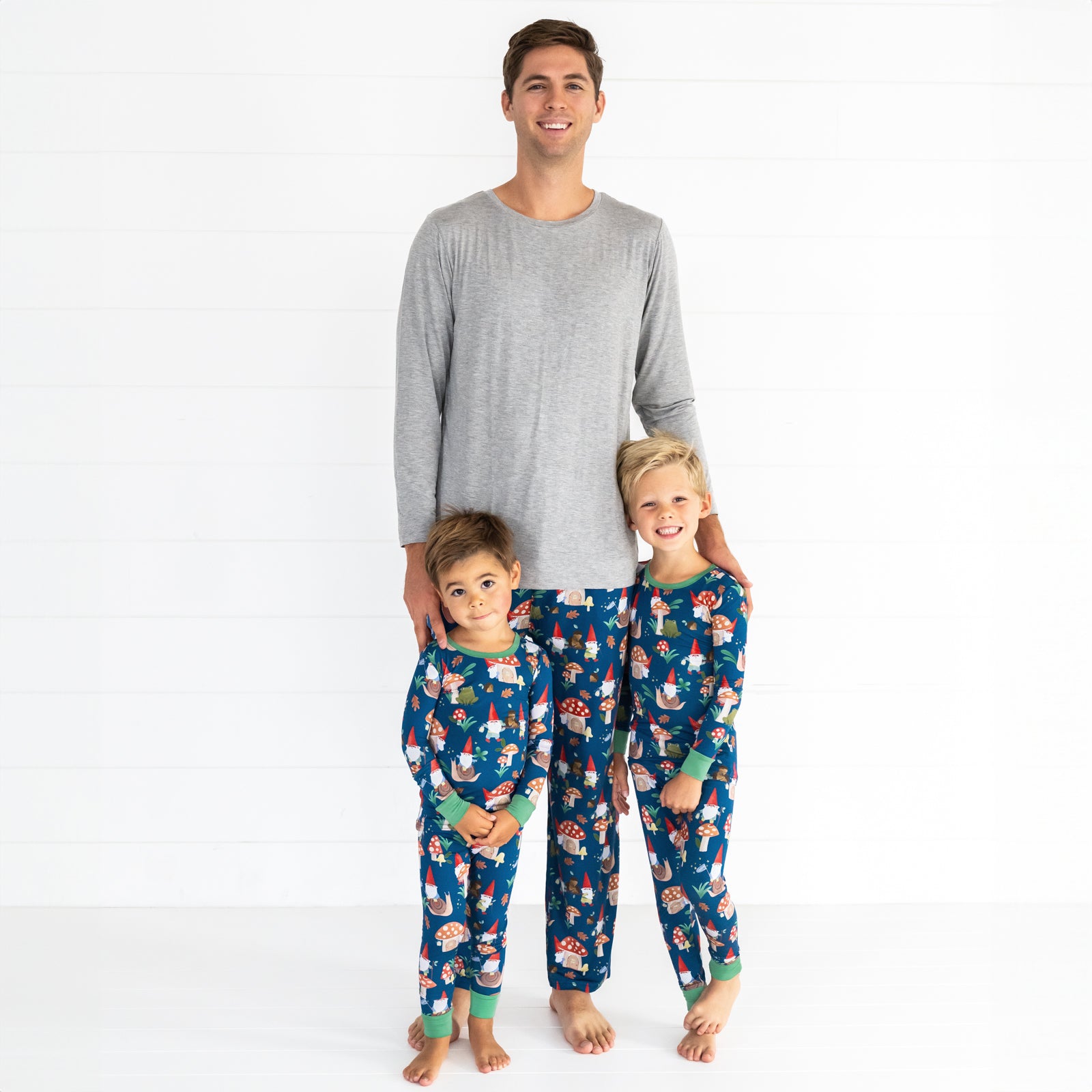 Family of three in the Forest Gnomes print. Both boys are in the Forest Gnomes Two-Piece Pajama Set and male model is wearing the Forest Gnomes Men's Pajama Pant