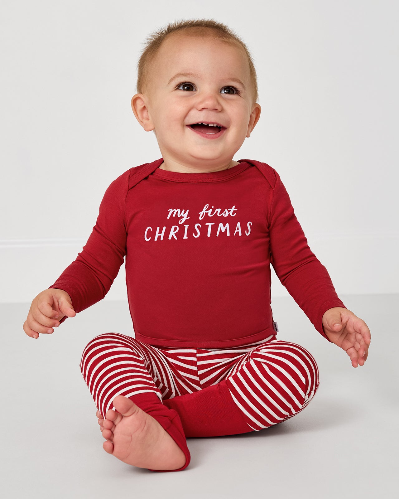 Baby wearing the My First Christmas Bodysuit with red striped leggings