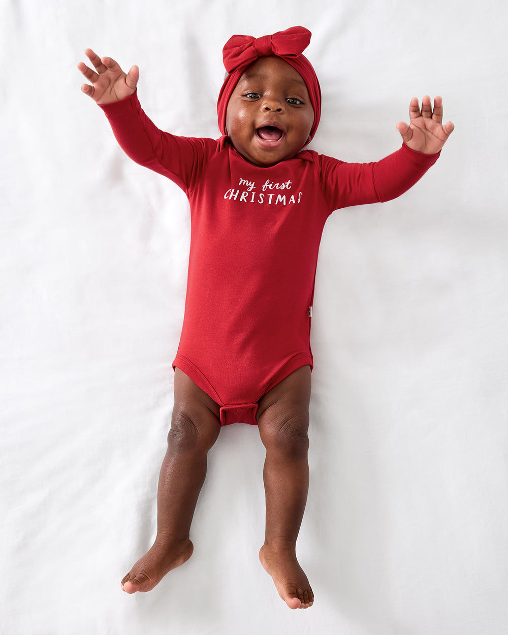 Aerial view of baby wearing the My First Christmas Bodysuit with a red bow headband