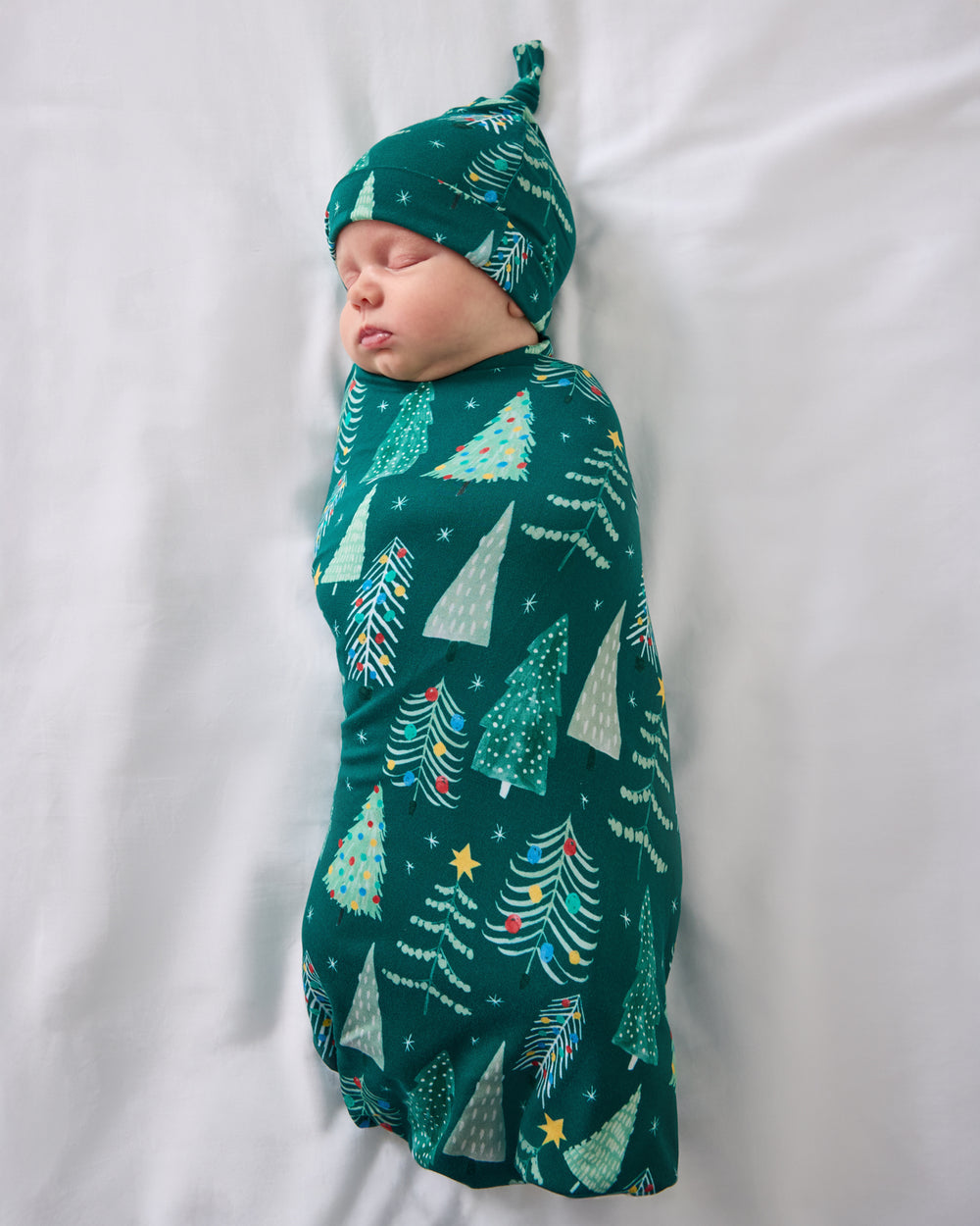 Aerial view of baby wearing the Twinkling Trees Swaddle & Hat Set