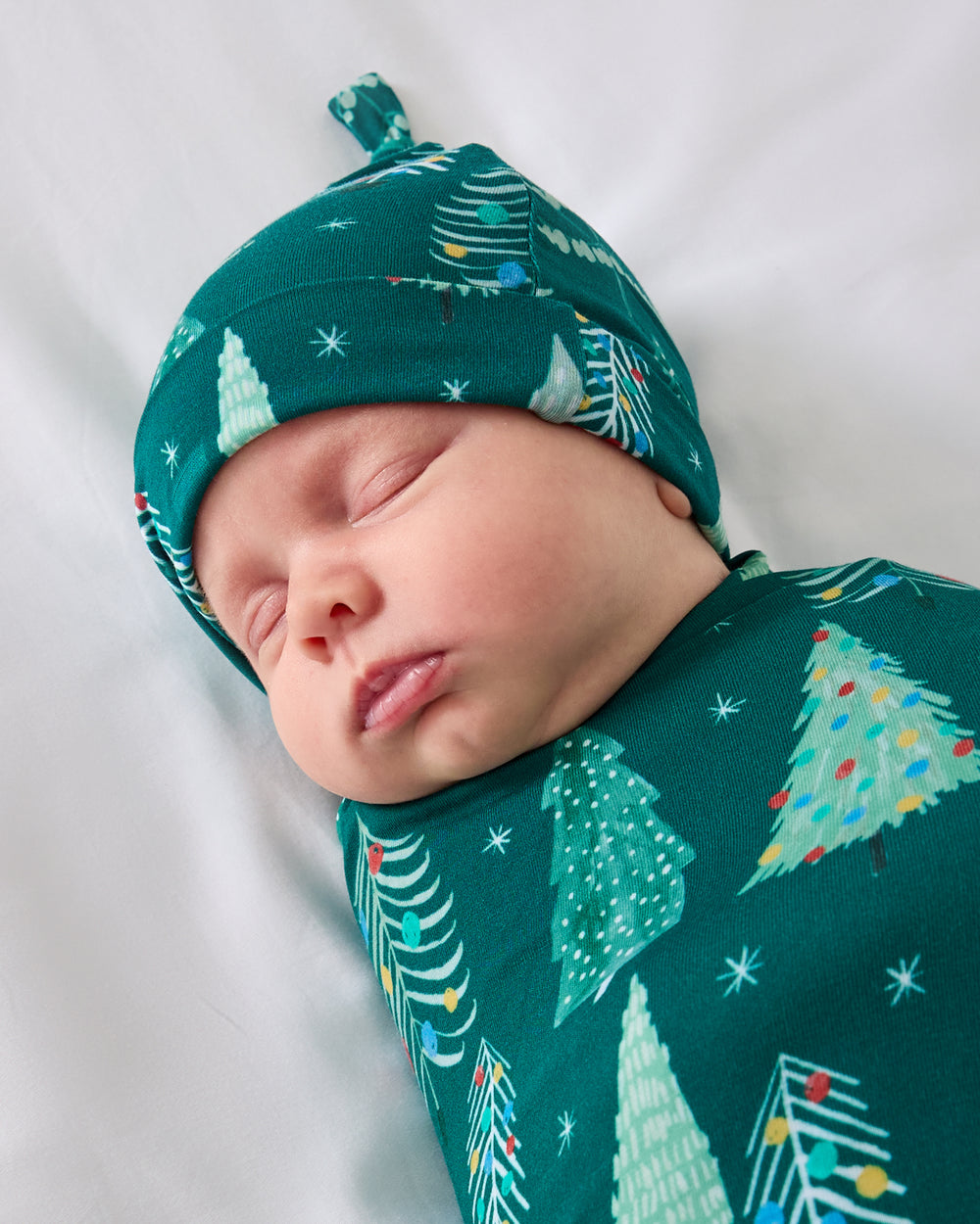 Close up of baby wearing the Twinkling Trees Swaddle & Hat Set