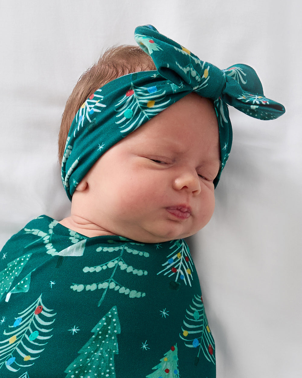 Close up of baby wearing the Twinkling Trees Swaddle & Luxe Bow Headband Set