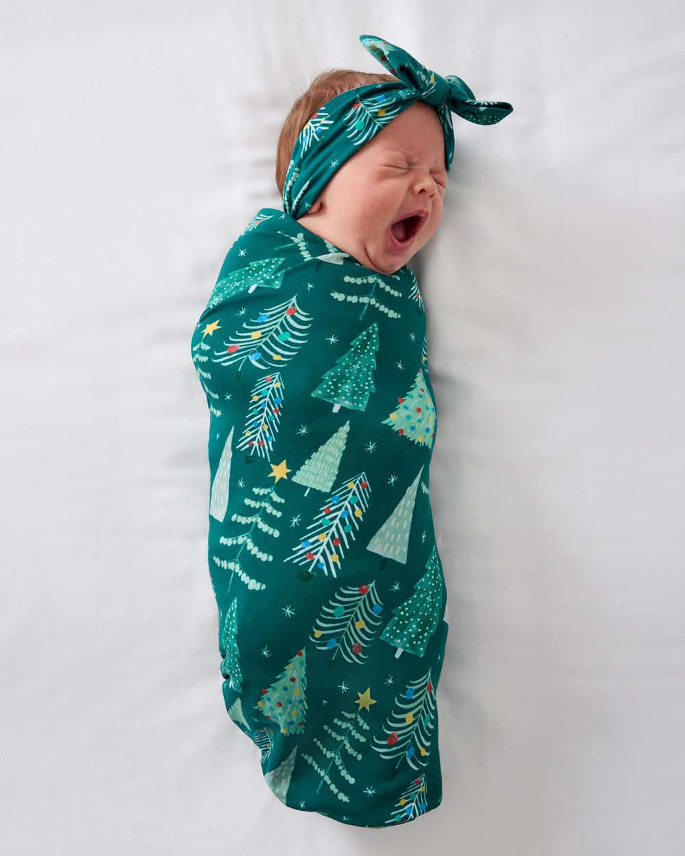 Aerial view of baby wearing the Twinkling Trees Swaddle & Luxe Bow Headband Set