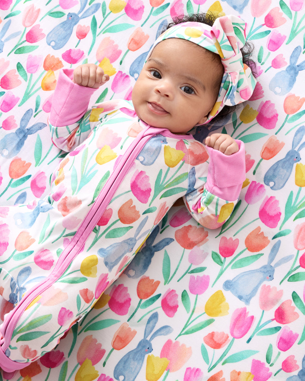 Baby laying on the Garden Hop Fitted Crib Sheet wearing a matching zippy