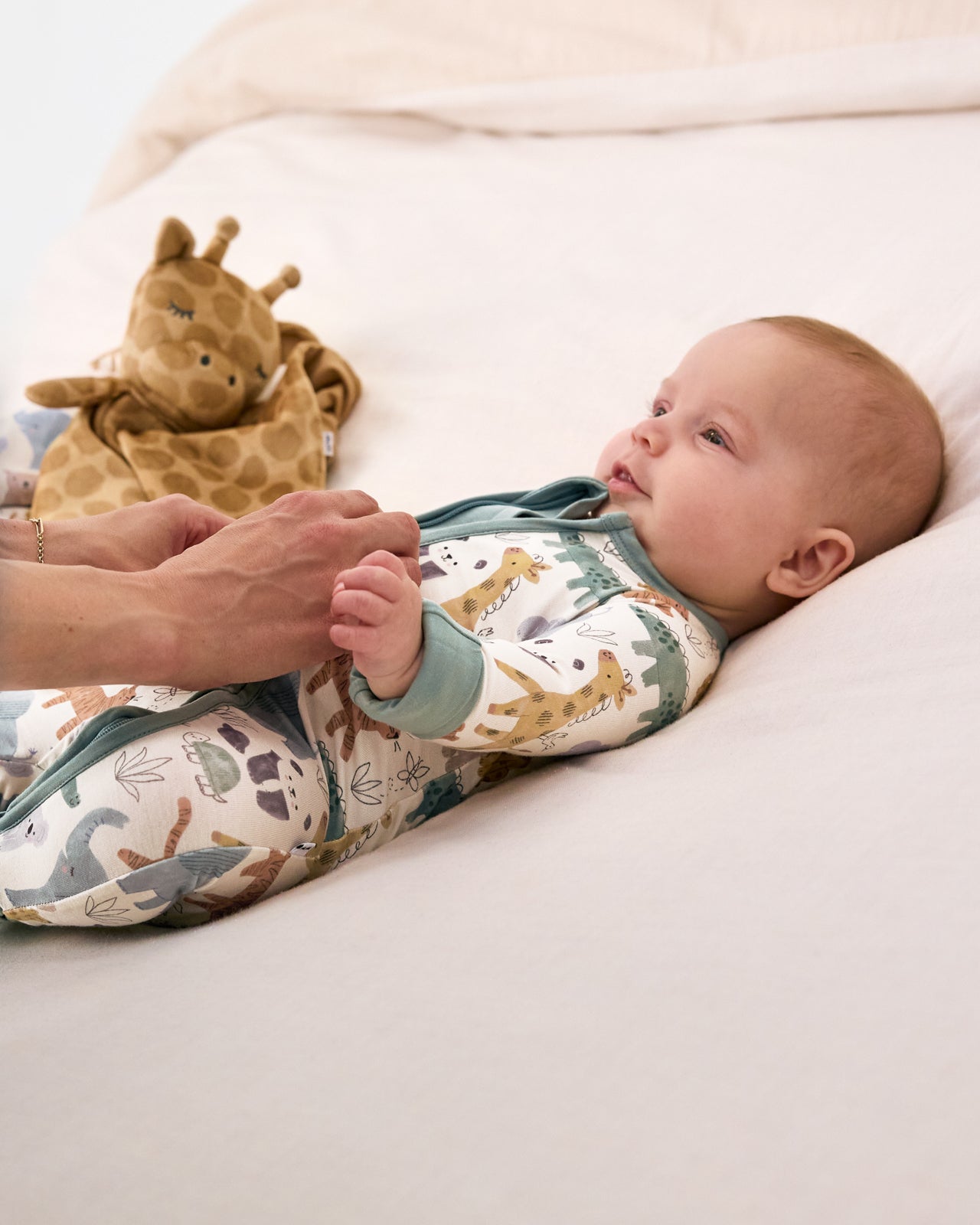 Baby laying on white bedding with the Giraffe Sleepyhead Lovey