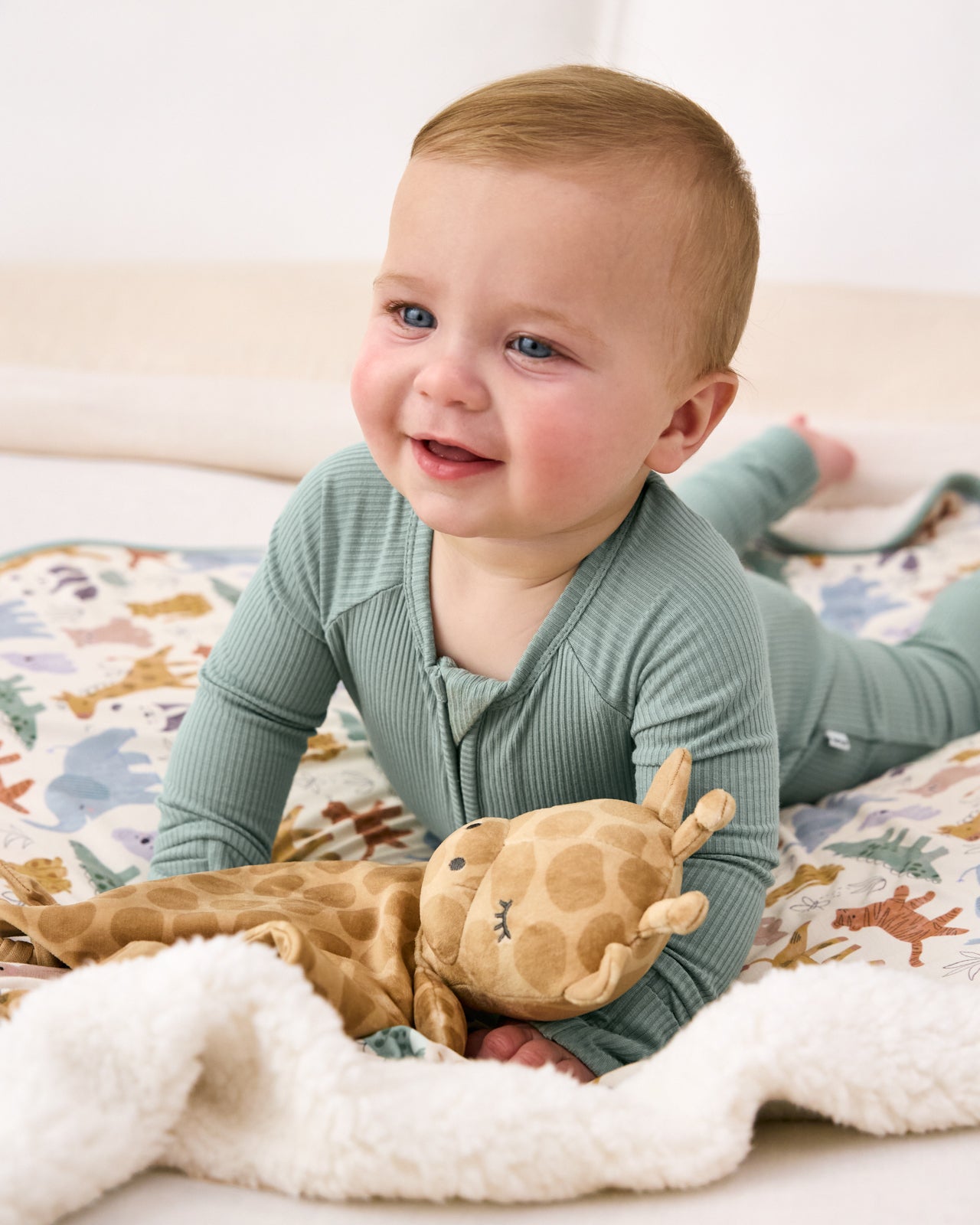 Baby laying on a safari themed baby blanket with the Giraffe Sleepyhead Lovey