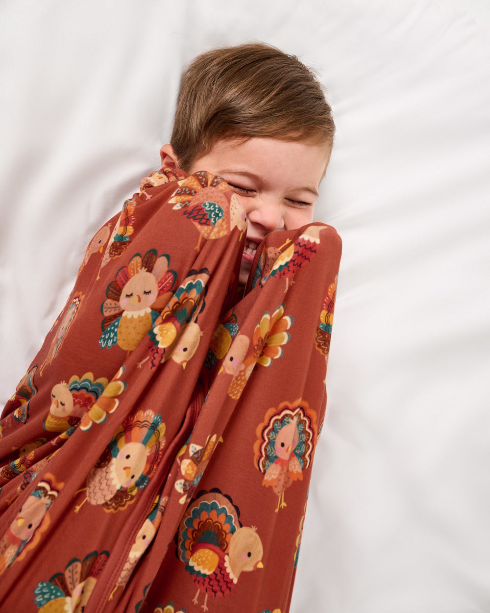 Aerial view of boy wrapped in the Grateful Gobbles Large Cloud Blanket® on a white bed